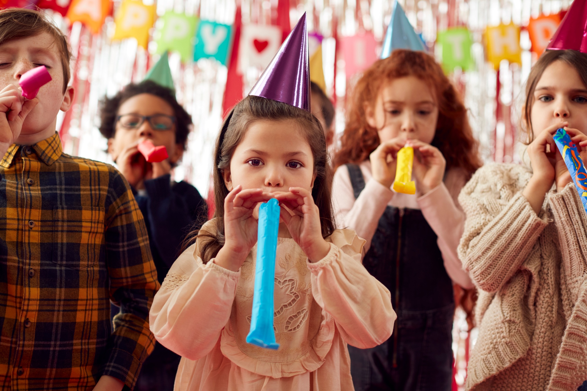 Group Of Children Celebrating At Birthday Party With Paper Hats And Party Blowers