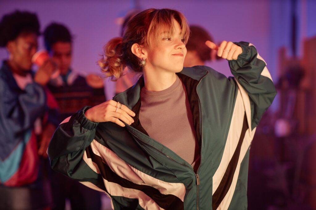 Young girl wearing retro outfit dancing at 80s disco party in pink lights